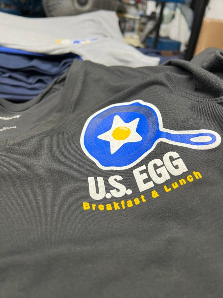 Close-up of a screen printed restaurant logo on a dark grey staff t-shirt